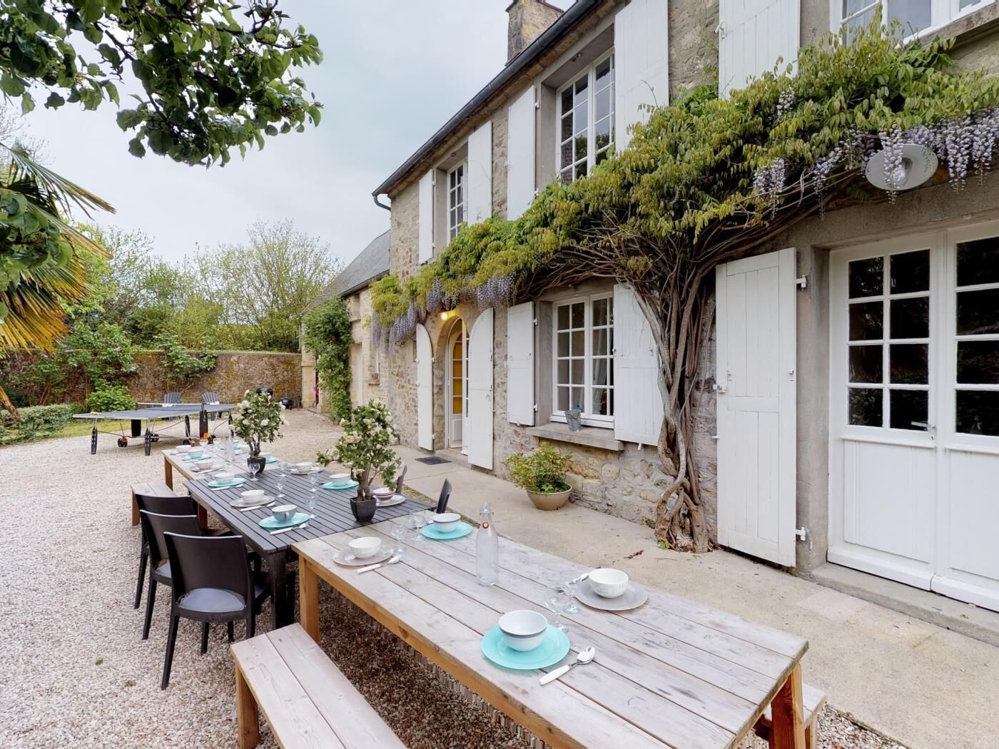 A stone building with a covered outdoor dining area, a large tree, and a gravel courtyard.