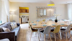 Una sala moderna con un sofá, una mesa de comedor lista para seis comensales y una cocina al fondo.