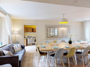 A modern living room with a sofa, a dining table set for six, and a kitchen in the background.