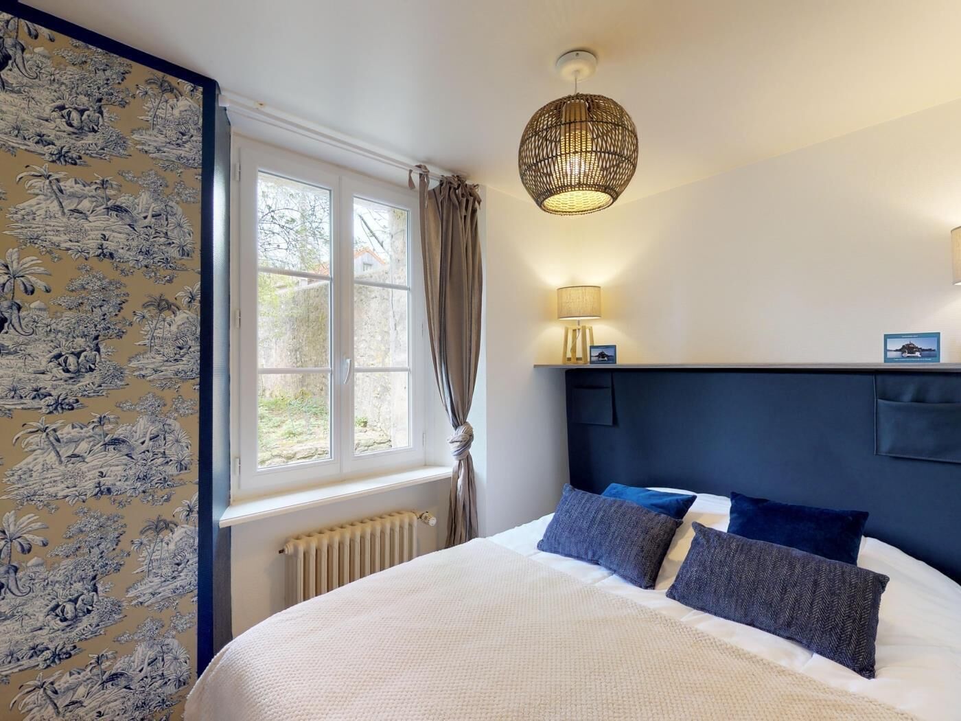 A bedroom with a large bed, a window with curtains, a wall-mounted lamp, and a decorative headboard.