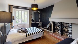 Un dormitorio con cama, una silla, una lámpara, chimenea y ventana.