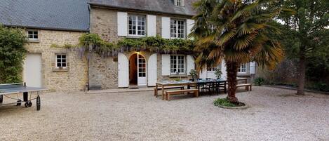 A stone building with a gravel courtyard, outdoor seating, and a palm tree.