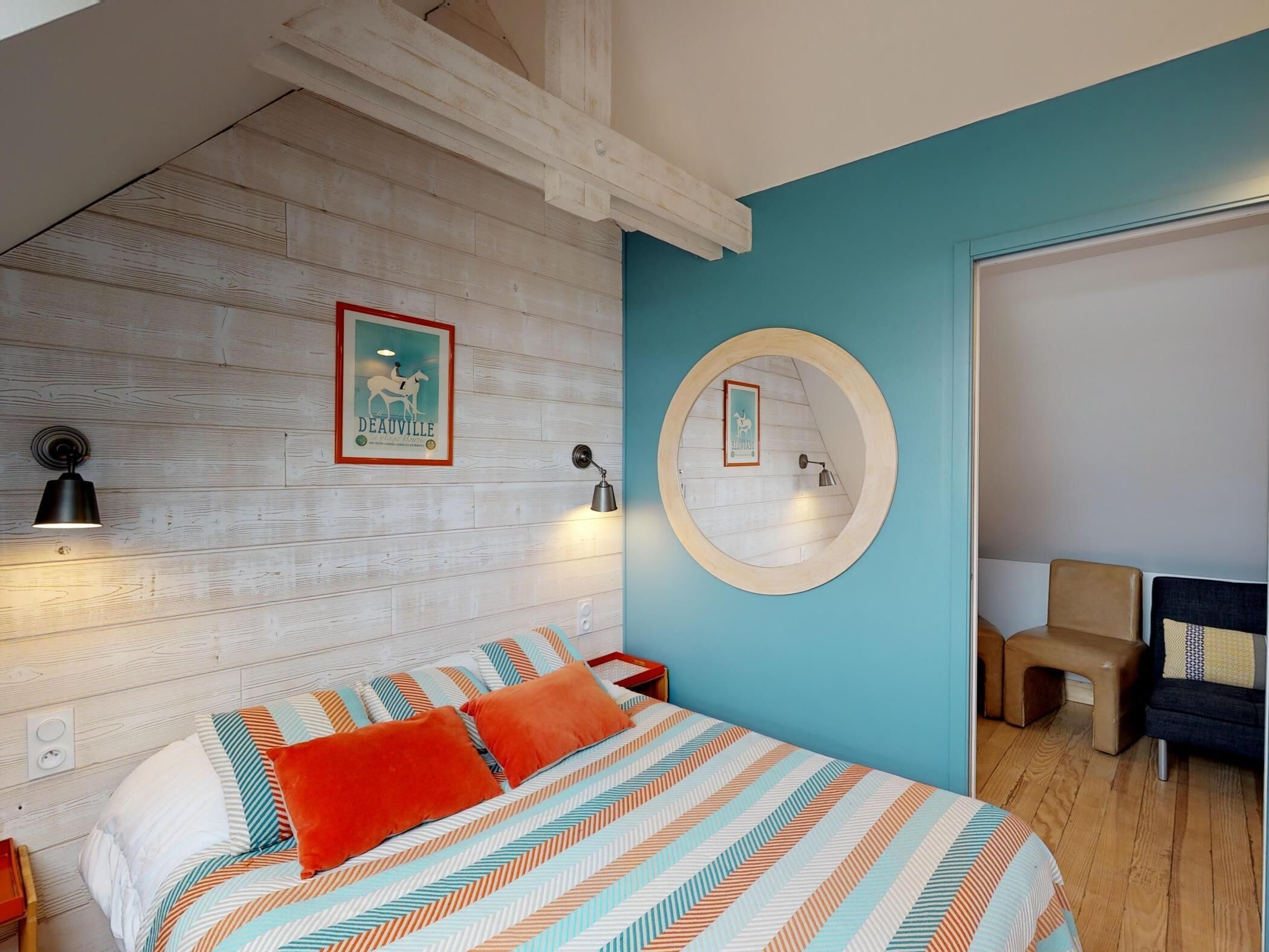 A bedroom with a bed, a round mirror, a wall-mounted lamp, and a framed picture.