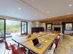 A conference room with a long table, red chairs, a laptop, and a fireplace.
