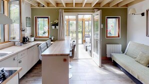 Une cuisine moderne dotée d’un îlot central, un coin repas avec une table et des chaises, un canapé et de grandes fenêtres qui laissent entrer la lumière naturelle.