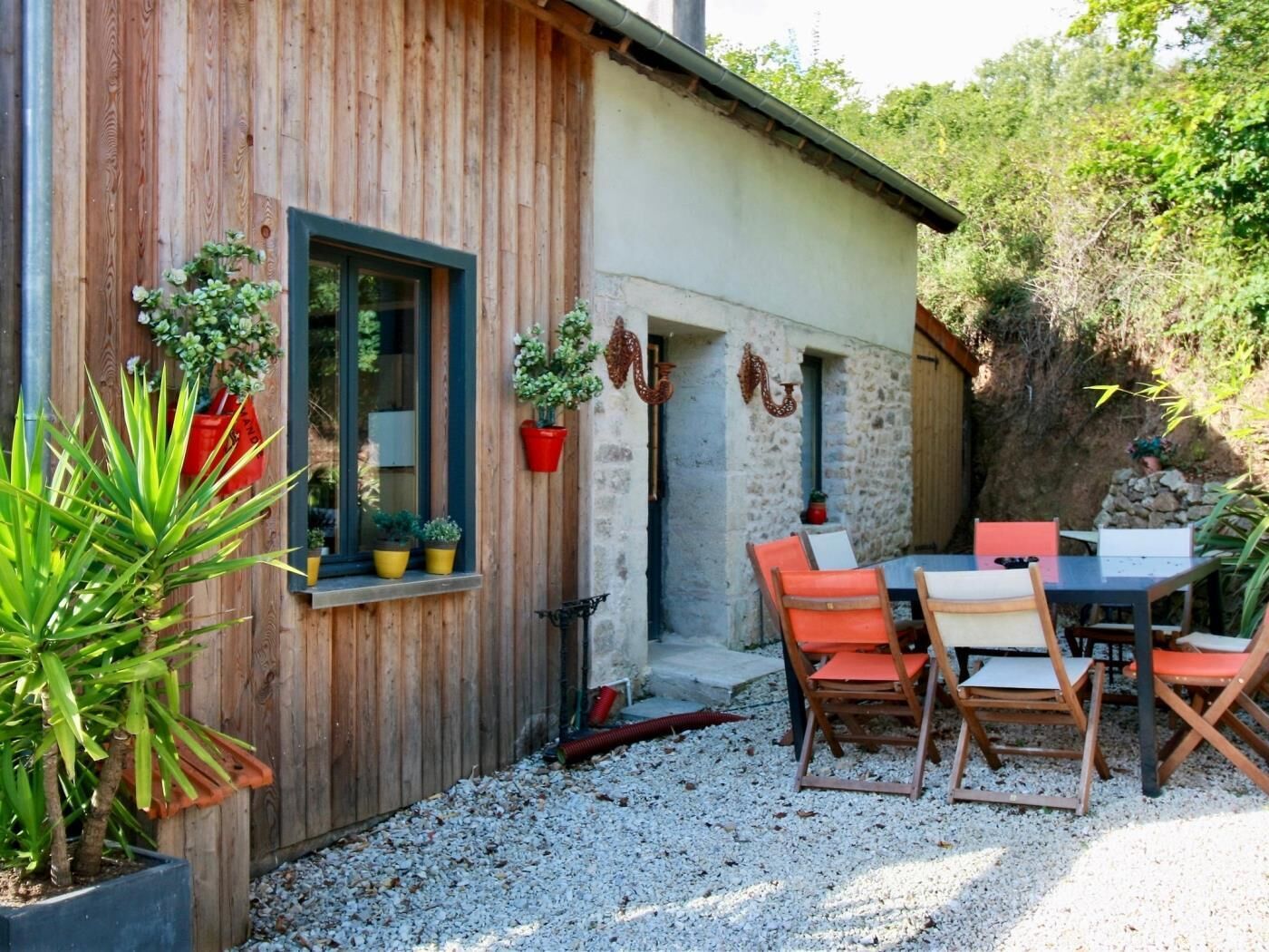 Un edificio rustico con facciata in legno, un muro in pietra e un patio sterrato con mobili da esterno.