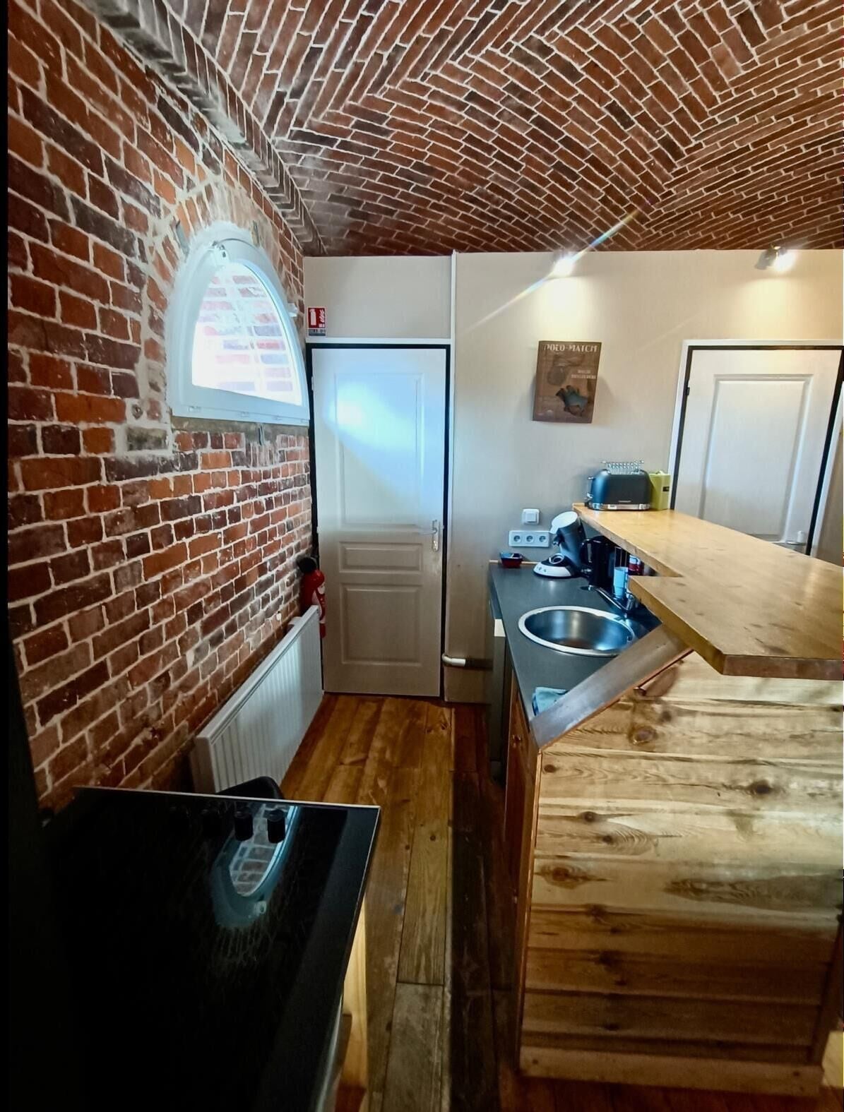 Une cuisine de taille réduite avec un mur en briques, une fenêtre, une porte et un comptoir en bois.