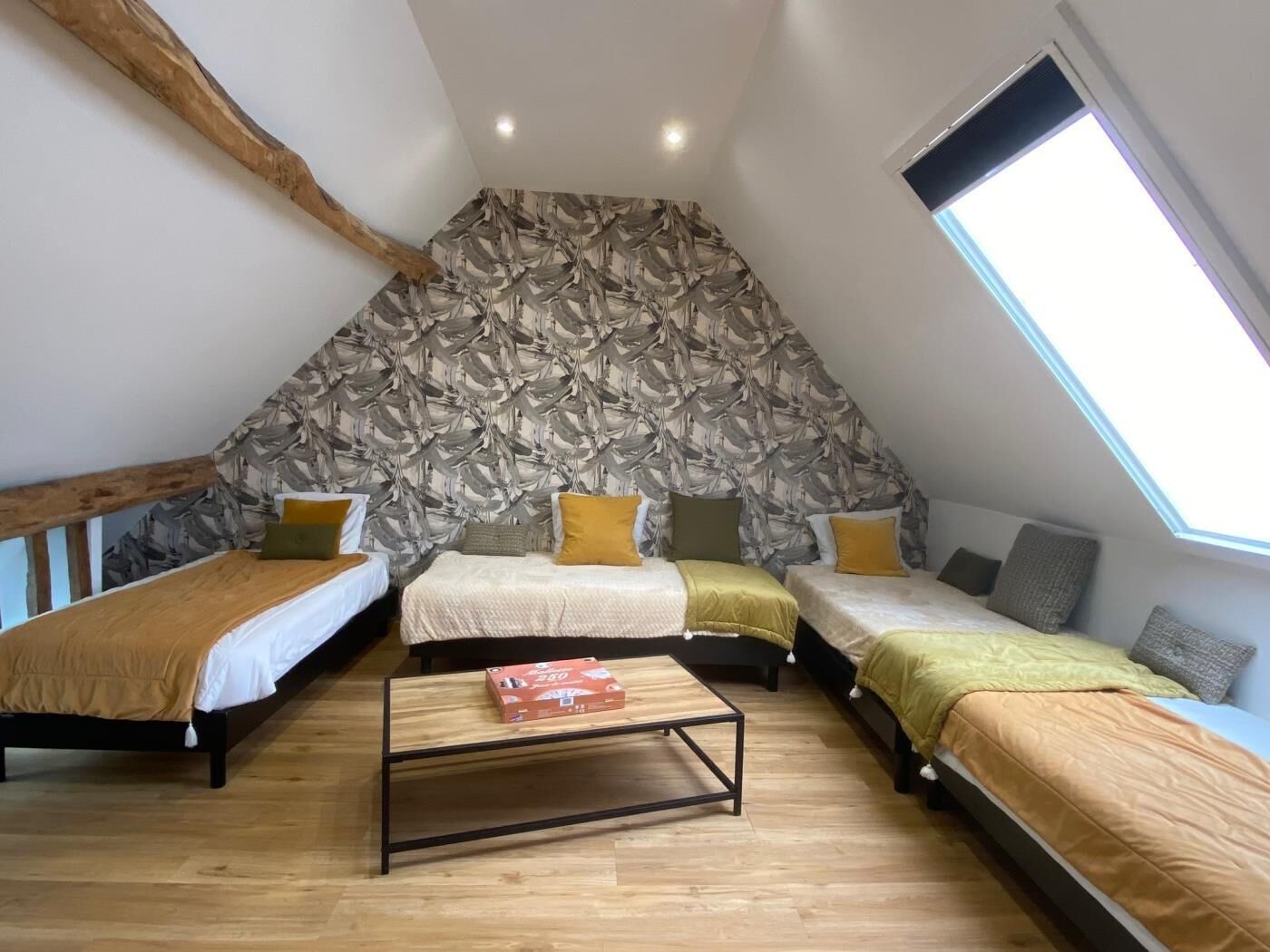 A triangular attic bedroom with three beds, a wooden table, and a sloped ceiling with a skylight.