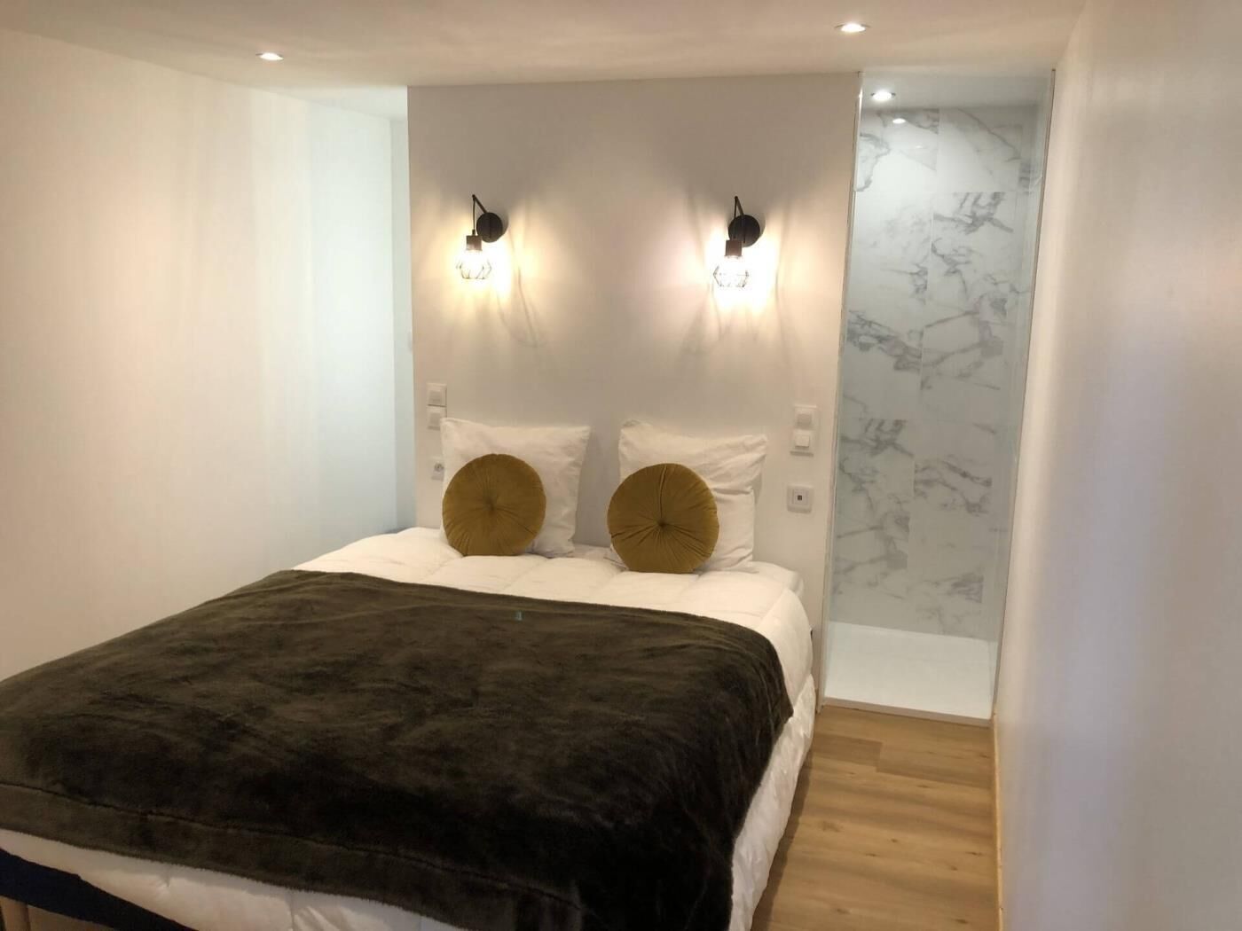 Un dormitorio con cama, dos luces empotradas, una pared de mármol y suelo de madera.