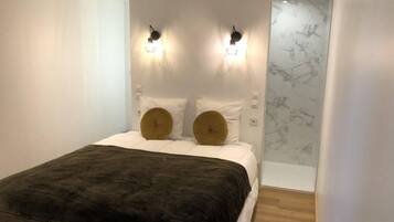 A bedroom with a bed, two wall-mounted lights, a marble wall, and a wooden floor.