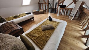 Ett loftliknande rum med två sängar, synliga träbjälkar, ett takfönster och en trappa.