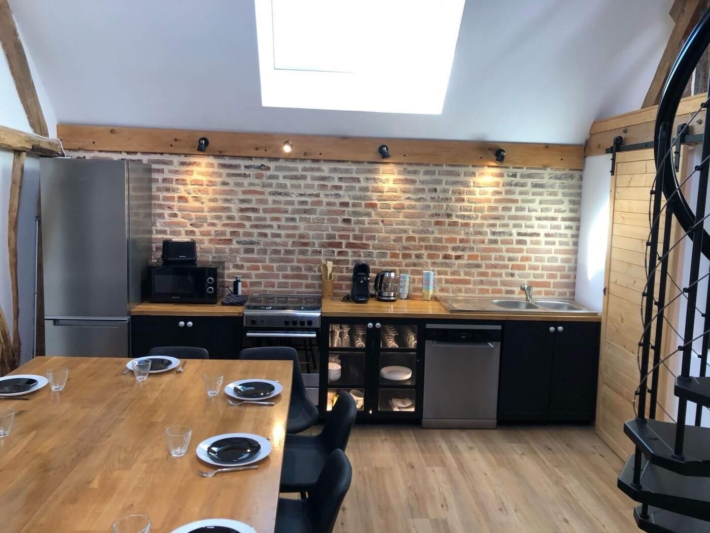 A compact kitchen with a brick wall, a skylight, a refrigerator, a stove, and a dishwasher.
