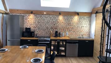 A compact kitchen with a brick wall, a skylight, a refrigerator, a stove, and a dishwasher.