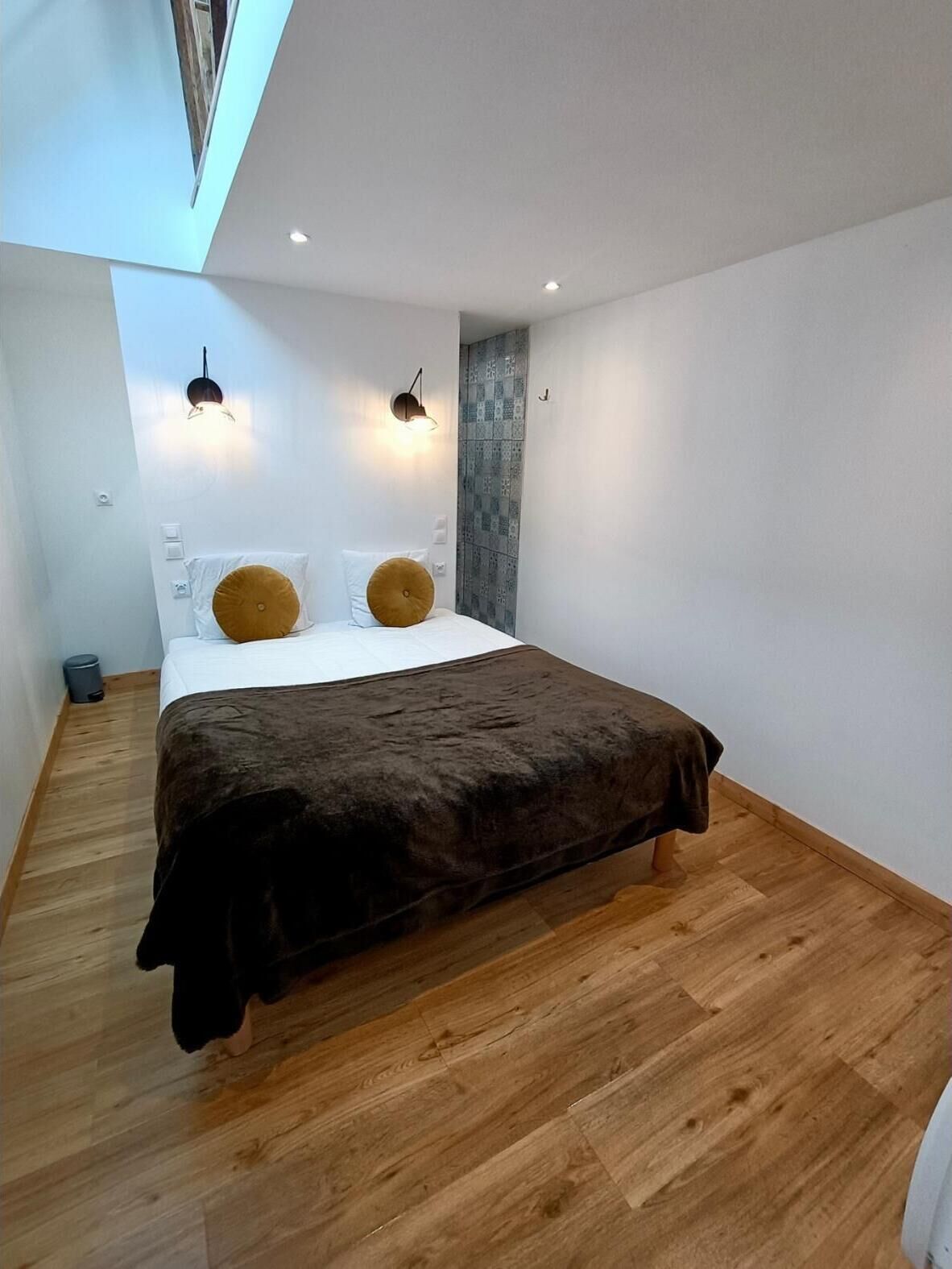 Un dormitorio con cama, dos luces fijadas a la pared, un papel tapiz estampado y suelo de madera.