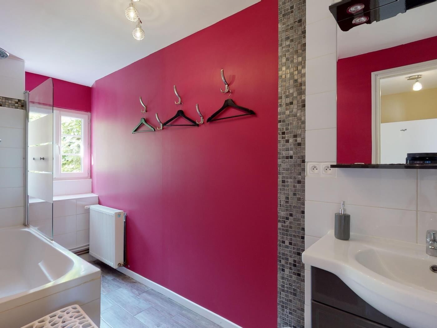 Un baño moderno con una pared roja, una bañera blanca, un lavabo con espejo y una zona de ducha.