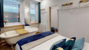 A bedroom with a bed, a bathtub, a window with curtains, and a mirror. - Cour du paradis 8 pers : billiards, baby, 30 min sea (Villedieu-les-Poêles)