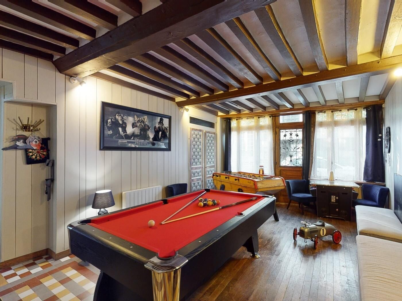 Une table de billard recouverte d’un drap de feutre rouge, une table de baby-foot et une queue de billard.