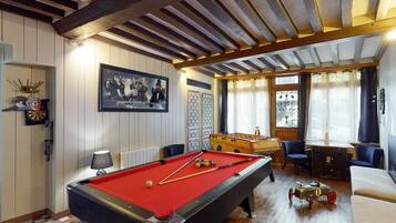 Une table de billard recouverte d’un drap de feutre rouge, une table de baby-foot et une queue de billard.