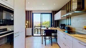 A modern kitchen with a built-in oven, a coffee machine, and a dining area with a table and chairs.