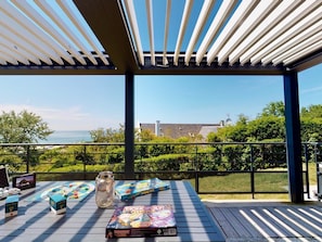 Un espace extérieur abrité avec vue sur la mer, une table avec des jeux de société et une bouteille.