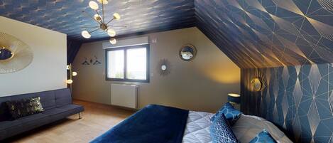 Une chambre avec un plafond en pente, un lit agrémenté d’oreillers à motifs, un canapé et une fenêtre.
