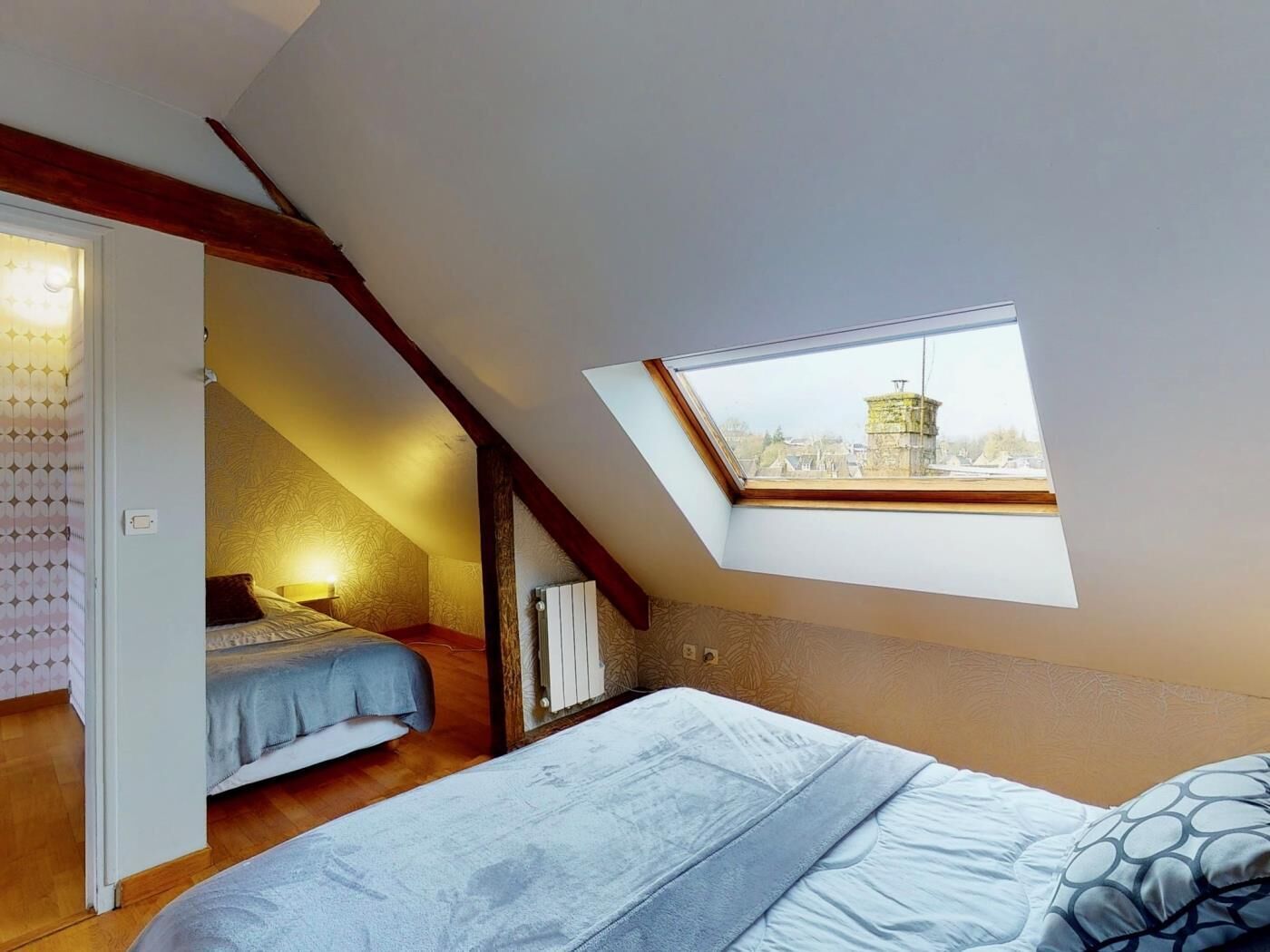 Un dormitorio con techo inclinado, tragaluz, cama, mesita de noche y radiador.
