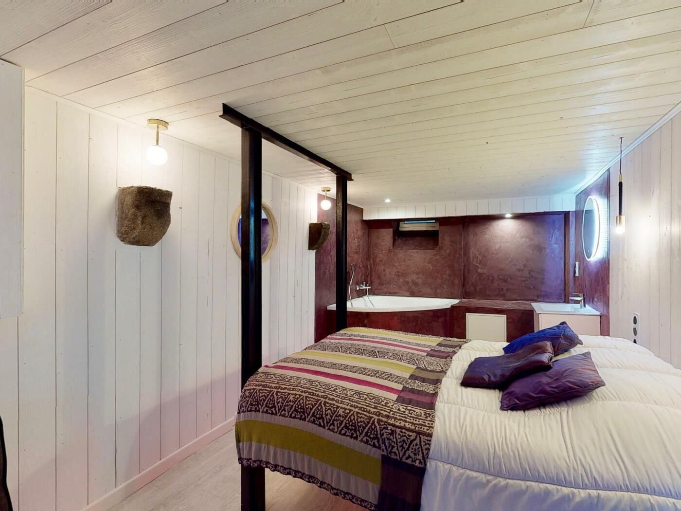 Une chambre à coucher avec un lit, un grand miroir, une coiffeuse avec un lavabo et une baignoire.