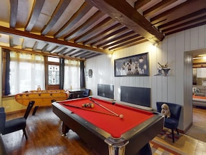 A pool table with a red felt surface, a billiards cue, and a pool ball. There is a wooden pool table with a vintage design in the background.