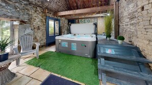 Een rustieke kamer met een stenen muur, houten plafond, een whirlpool, een stoel en een klein tafeltje met een plant.