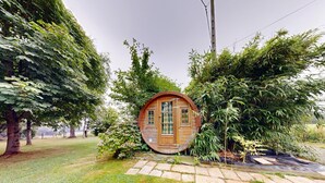 Een houten vakantiehuis met een ronde vorm, omringd door weelderige begroeiing en bomen.