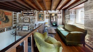 Un intérieur rustique avec des poutres apparentes, un canapé recouvert d’un tissu vert, une table en bois et un mur en pierre.