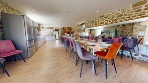 Un vaste espace dédié à la salle à manger, avec une longue table, de nombreuses chaises et un mur en pierre.