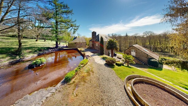 Un paysage rural avec un petit bâtiment, un ruisseau et un ciel dégagé.
