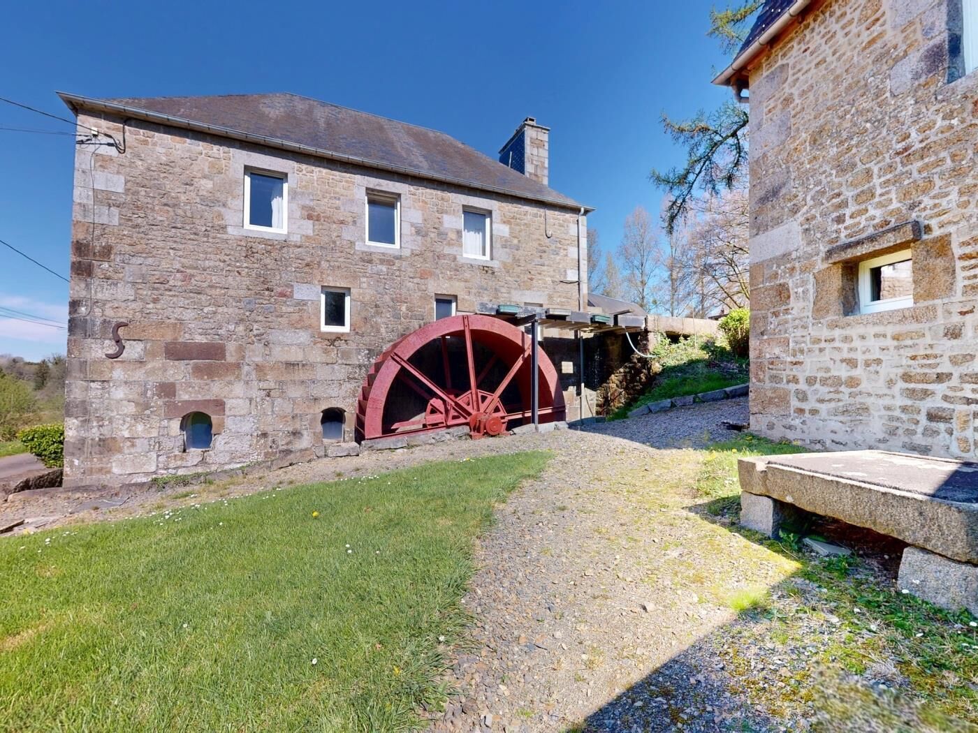Un bâtiment en pierre doté d’une grande roue à eau, d’un chemin de gravier et d’une zone herbeuse.