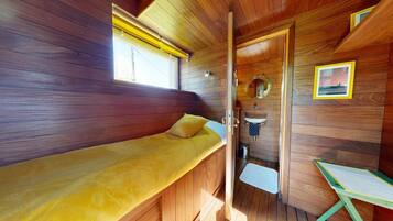 A compact cabin with a single bed, a small bathroom, and a window.