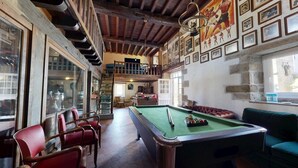 Une salle de billard équipée d’une table de billard, de chaises rouges, d’un canapé vert et d’un escalier menant à un niveau supérieur.