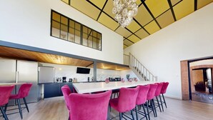 Una cocina moderna con una isla central, un comedor con sillas rojas y una escalera que sube a un nivel superior.