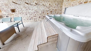 Una habitación con paredes de piedra, bañera de hidromasaje, terraza de madera y mobiliario exterior.