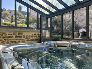 Ein Whirlpool mit Glasumrandung, Steinwänden und Blick auf einen Garten sowie Gebäude.