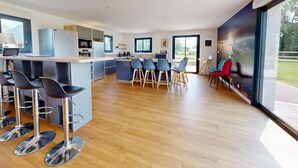A modern kitchen with a central island, bar stools, and a dining area with chairs. - Concorde Aérogare 25 people 2 Cottage : jacuzzi baby airhockey (La Haye-Pesnel)