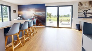 A modern kitchen with a large window, a wooden countertop, and bar stools. - Concorde Aérogare 25 people 2 Cottage : jacuzzi baby airhockey (La Haye-Pesnel)