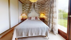 Ein Schlafzimmer mit einem großen Bett, zwei Nachttischlampen, einem Himmelbett und Blick ins Freie.