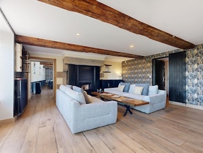 A spacious living area with a fireplace, two sofas, a wooden coffee table, and exposed wooden beams on the ceiling.