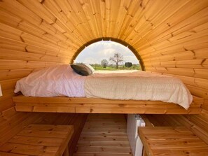 A circular wooden room with a bed centered under a large arched window.
