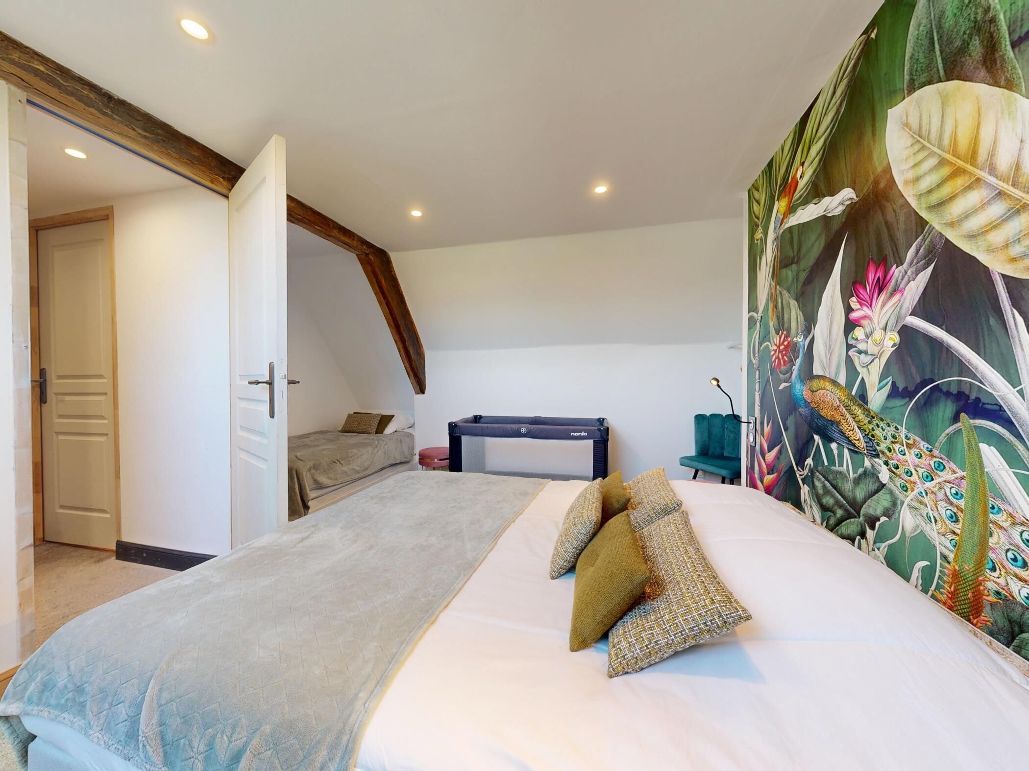 Une chambre à coucher avec un lit, un banc, une porte et un mur orné d’une fresque florale.