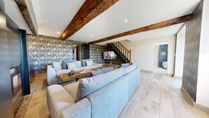 A modern living room with a large L-shaped sofa, a wooden coffee table, and a staircase leading to an upper level. - Auberge St Vincent Diligence 35 people 2 Cottage : jacuzzi games (Braffais – Le Parc)