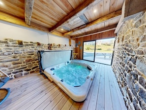 A hot tub in a wooden cabin with stone walls and a view of the outdoors.