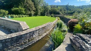 Un mur de pedra, una zona verda i un canal d'aigua.