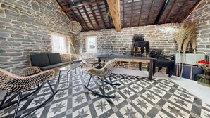 Un interior rústic amb parets de pedra, sostre de fusta, terra amb dibuixos i zona de menjador amb cadires i taula.