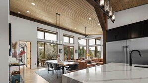 A modern kitchen with a large island, a dining area with a wooden table and chairs, and a cozy seating area with a sofa and cushions. - Mountain Modern Retreat w/Hot Tub (Victor)